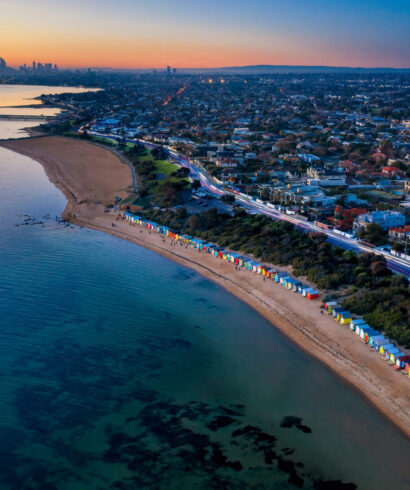 Aerial sunset view of the iconic bathing huts on Brighton beach, with St Kilda Marina and the city of Melbourne in the distance, captured at dusk
